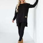 Person wearing a black outfit with beige boots against a white wall.