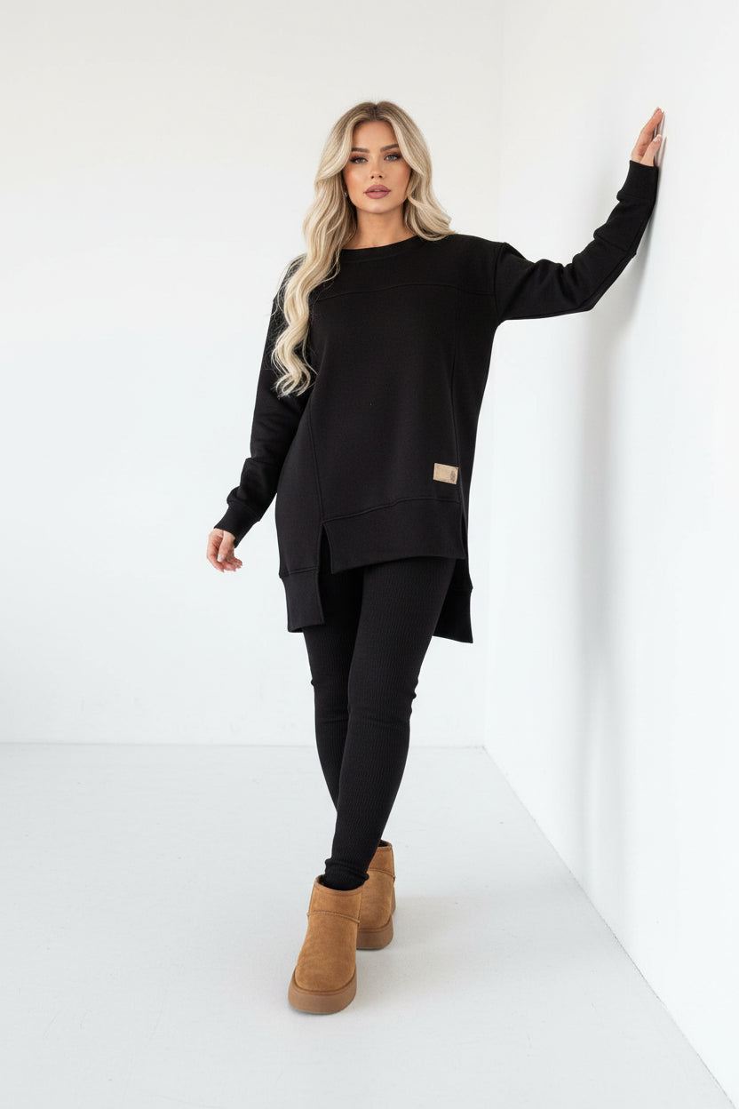 Person wearing a black outfit with beige boots against a white wall.