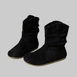 Black suede boots on a textured surface with a laptop in the background