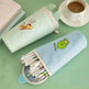 Pencil case with cartoon design on a green surface with a cup of coffee.