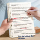 A spiral-bound notebook shown being held open by two hands, with a pen writing on a page. The pages are folded in half to demonstrate a 360-degree fold, with text at the bottom reading 'Fold in half and hold the pages' and 'Can be folded 360 degrees.