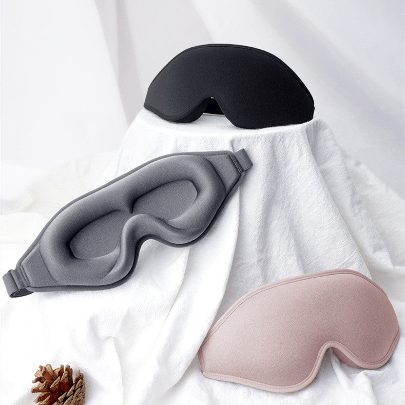 Three sleep masks in black, gray, and pink on a white fabric background.