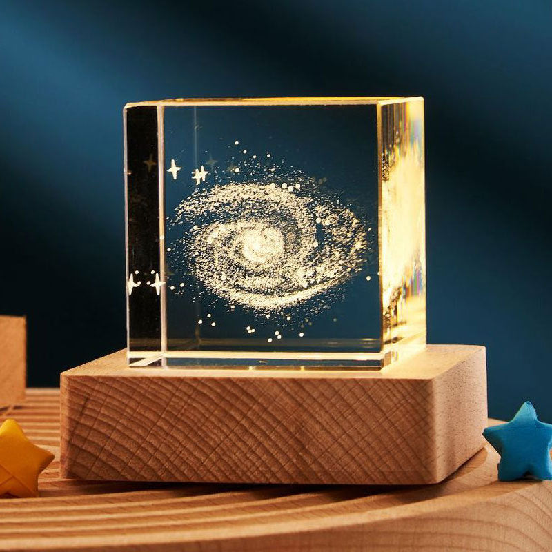 Glass block with galaxy design on a wooden base against a dark background