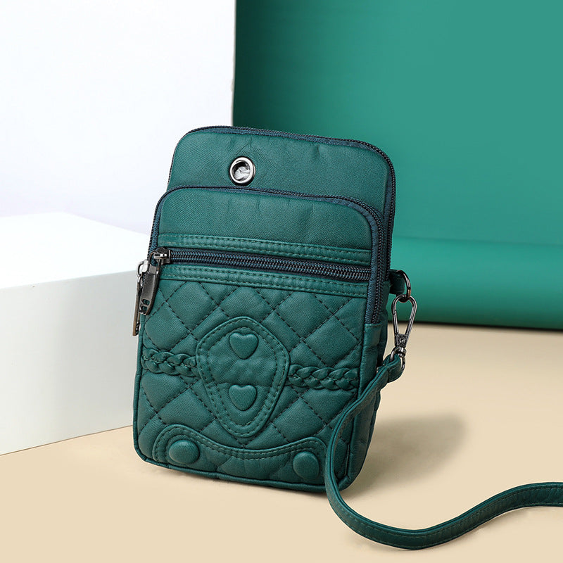 Teal quilted crossbody bag with heart patterns on a beige surface with a green background