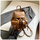 Brown leather backpack on a bed with a book and gray fabric