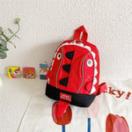 Red children's backpack with a shark design on a white wall.