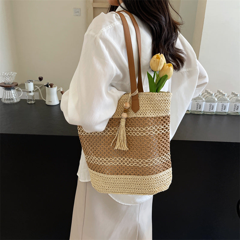 Person holding a woven handbag with a tassel and flowers, standing in a room.
