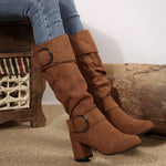 Brown knee-high boots with buckles worn by a person sitting on a wooden bench.