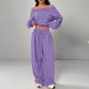 Person wearing a purple off-shoulder top and wide-leg pants on a gray background
