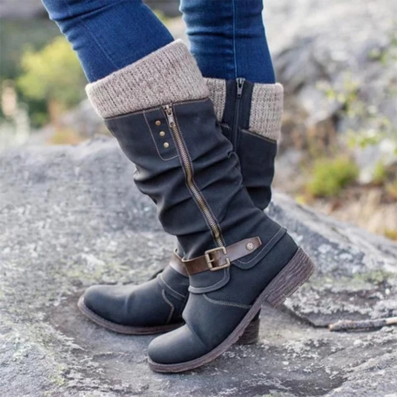 Blue knee-high boots with brown buckles worn by a person on a rocky surface.