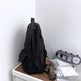 Black backpack on a wooden surface with a white wall background