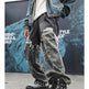 A person wearing distressed gray camouflage jeans, a blue denim jacket, and black high-top boots with white bandana prints and silver studs, standing in front of a dark blue graphic backdrop.