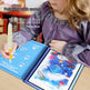 Child using a water-soluble ink pen to draw on a coloring book with underwater-themed illustrations.