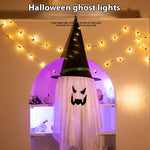 Halloween ghost decoration with a black hat and string lights on a wall.