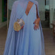 Woman in a light blue dress holding a woven handbag indoors.