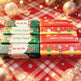 Four pairs of Christmas-themed candy bars arranged in a 2x2 grid on a red and white checkered blanket with warm holiday lights and ornaments in the background. The left pair has green, white, and dark green wrappers with 'Ho Ho Ho' and 'Santa Claus' text and Santa illustrations.
