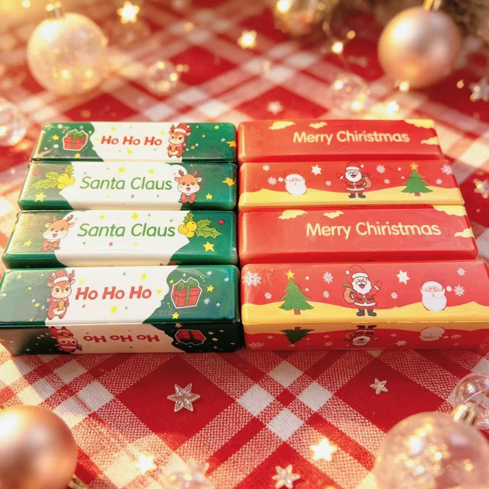 Four pairs of Christmas-themed candy bars arranged in a 2x2 grid on a red and white checkered blanket with warm holiday lights and ornaments in the background. The left pair has green, white, and dark green wrappers with 'Ho Ho Ho' and 'Santa Claus' text and Santa illustrations.