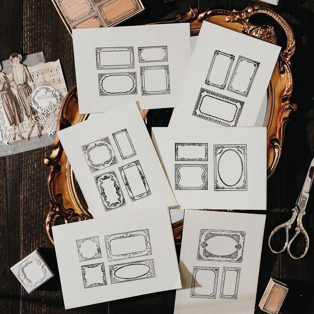 Sheets of decorative paper with ornate frames on a wooden surface with scissors.