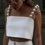 Woman wearing a white strapless top with pearl-like shoulder details.