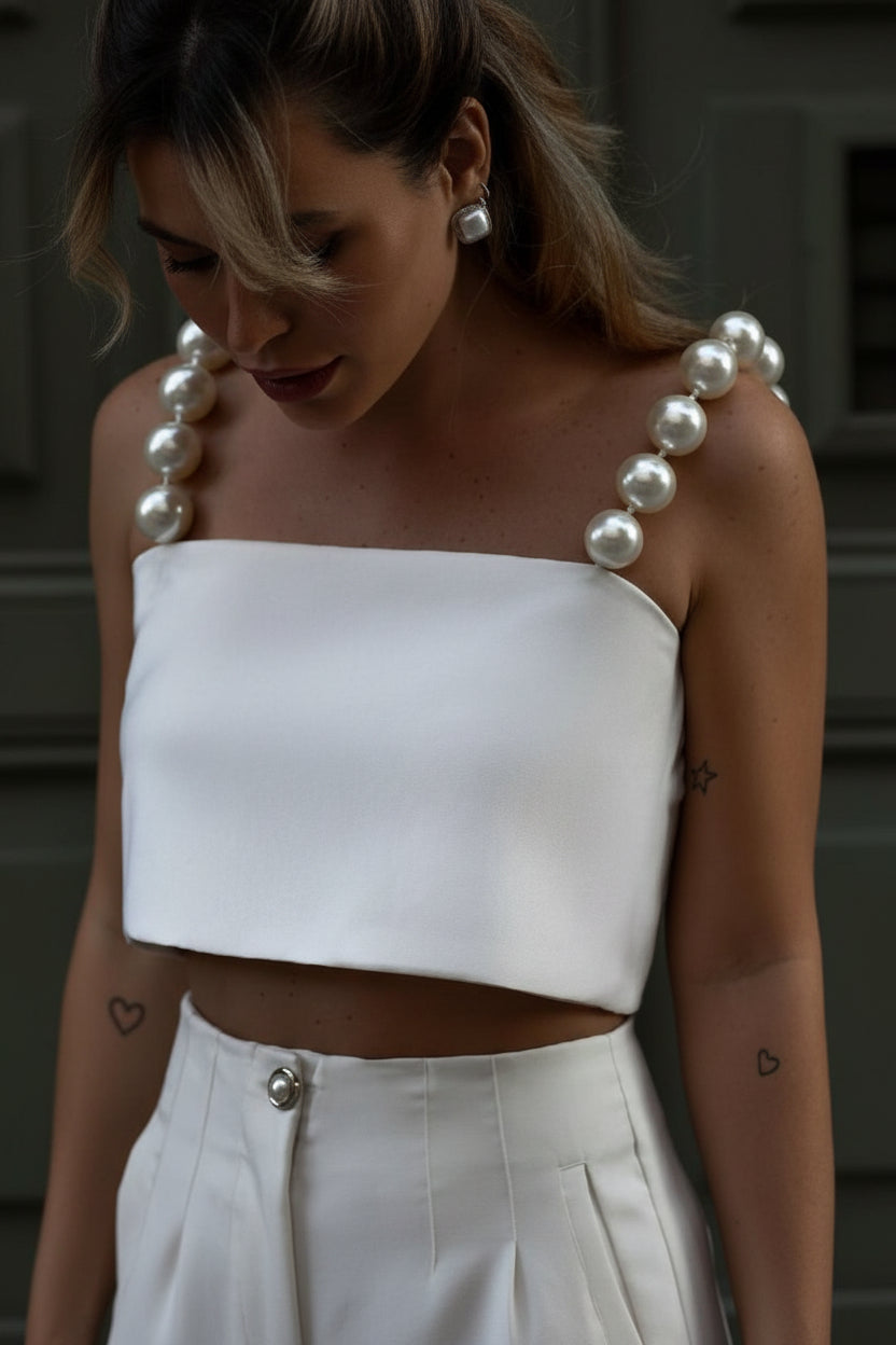 Woman wearing a white strapless top with pearl-like shoulder details.