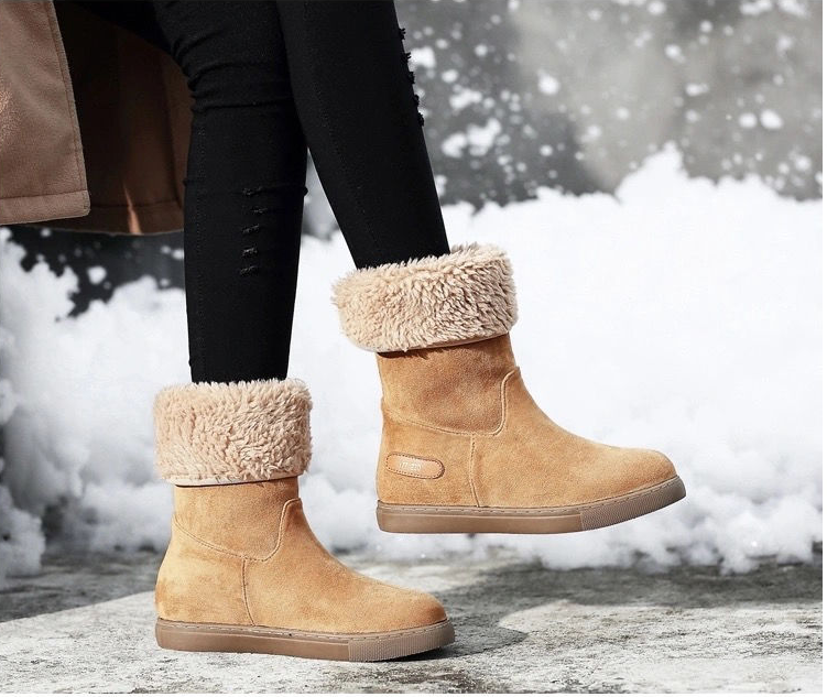 Tan winter boots with fur trim worn by a person on a snowy ground.