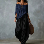 A woman models an off-the-shoulder navy blue top and black wide-leg harem pants against a textured gray studio backdrop.