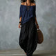 A woman models an off-the-shoulder navy blue top and black wide-leg harem pants against a textured gray studio backdrop.