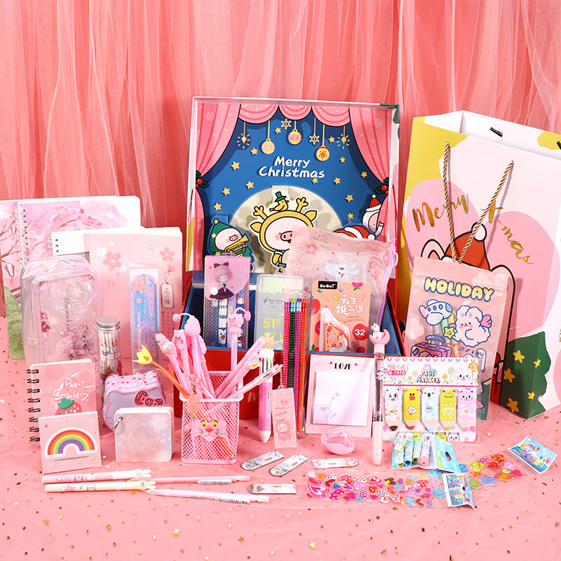 Assorted stationery items on a pink surface with a Christmas-themed card in the background.