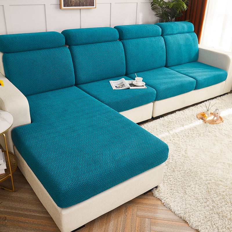 A sectional sofa with bright teal textured seat and back cushions and cream-colored arms, base, and side panels, shown in a styled living room with a white shag rug, wood floor, and small side table.