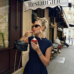 Woman in a polka dot dress eating ice cream outside a restaurant.