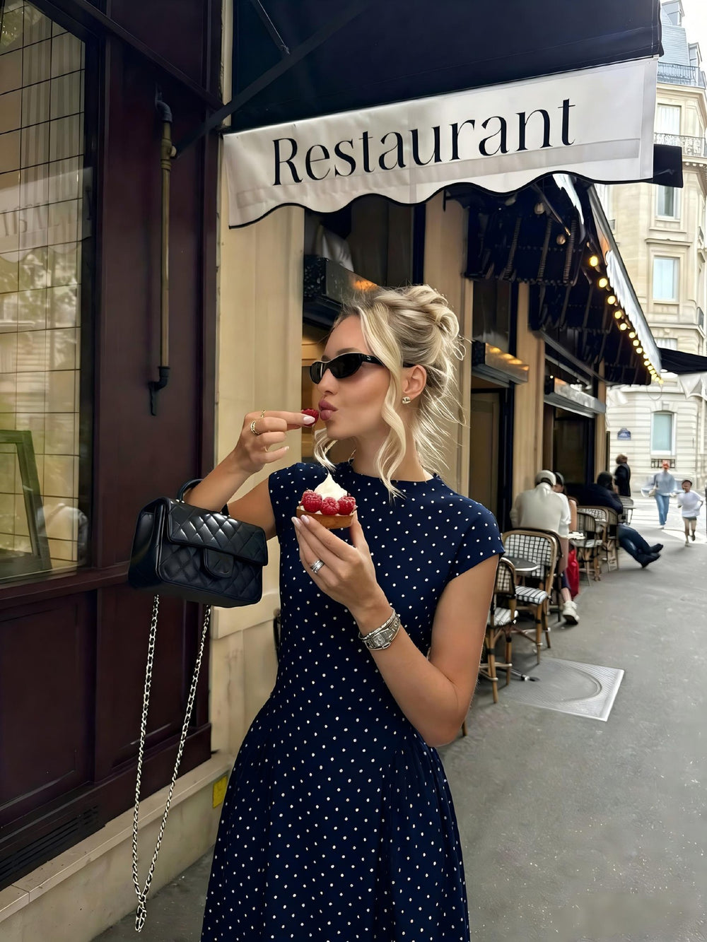 Woman in a polka dot dress eating ice cream outside a restaurant.