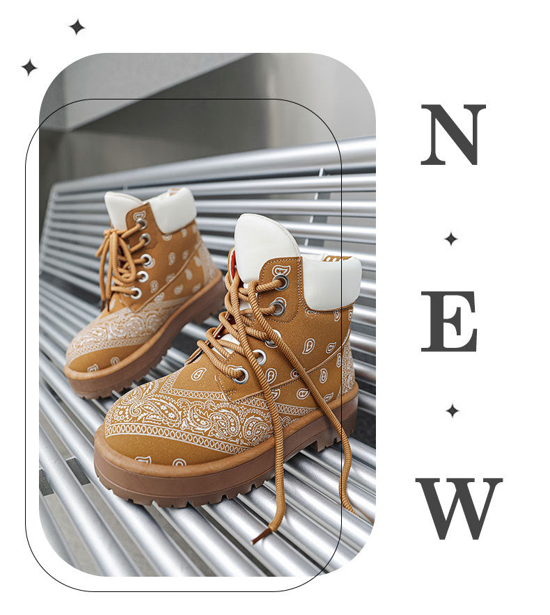 A pair of tan lace-up ankle boots with white bandana paisley prints on the sides, white faux-fur collars, and brown soles, displayed on a metallic roller conveyor. The image has a stylized border and the text 'NEW' printed vertically on the right.