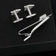Silver cufflinks and tie clip on a black background