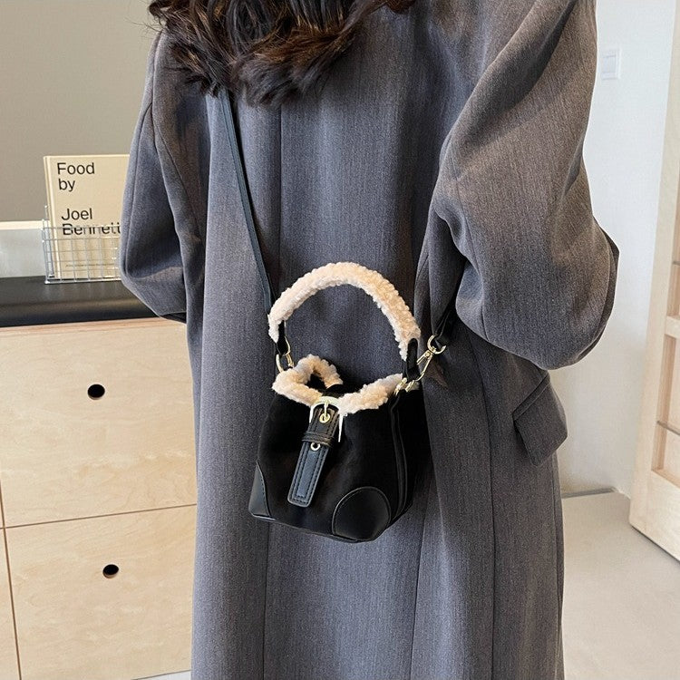 Person wearing a gray coat with a black handbag featuring white fur trim.