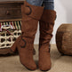 Brown knee-high boots with decorative buckles worn by a person, with a wooden drawer and basket in the background.