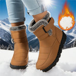 Brown winter boots with fur trim worn in the snow, with a mountainous background.