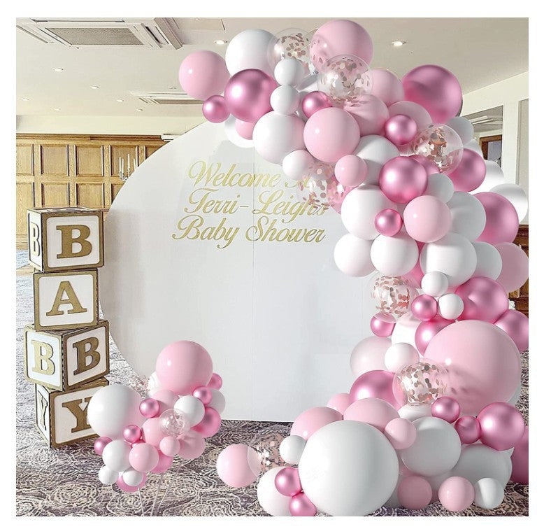 Pink, white, and silver balloon garland arch decoration with a large white round backdrop featuring gold script text reading 'Welcome to Jerris-Leger Baby Shower,' plus stacked wooden baby blocks on the left.