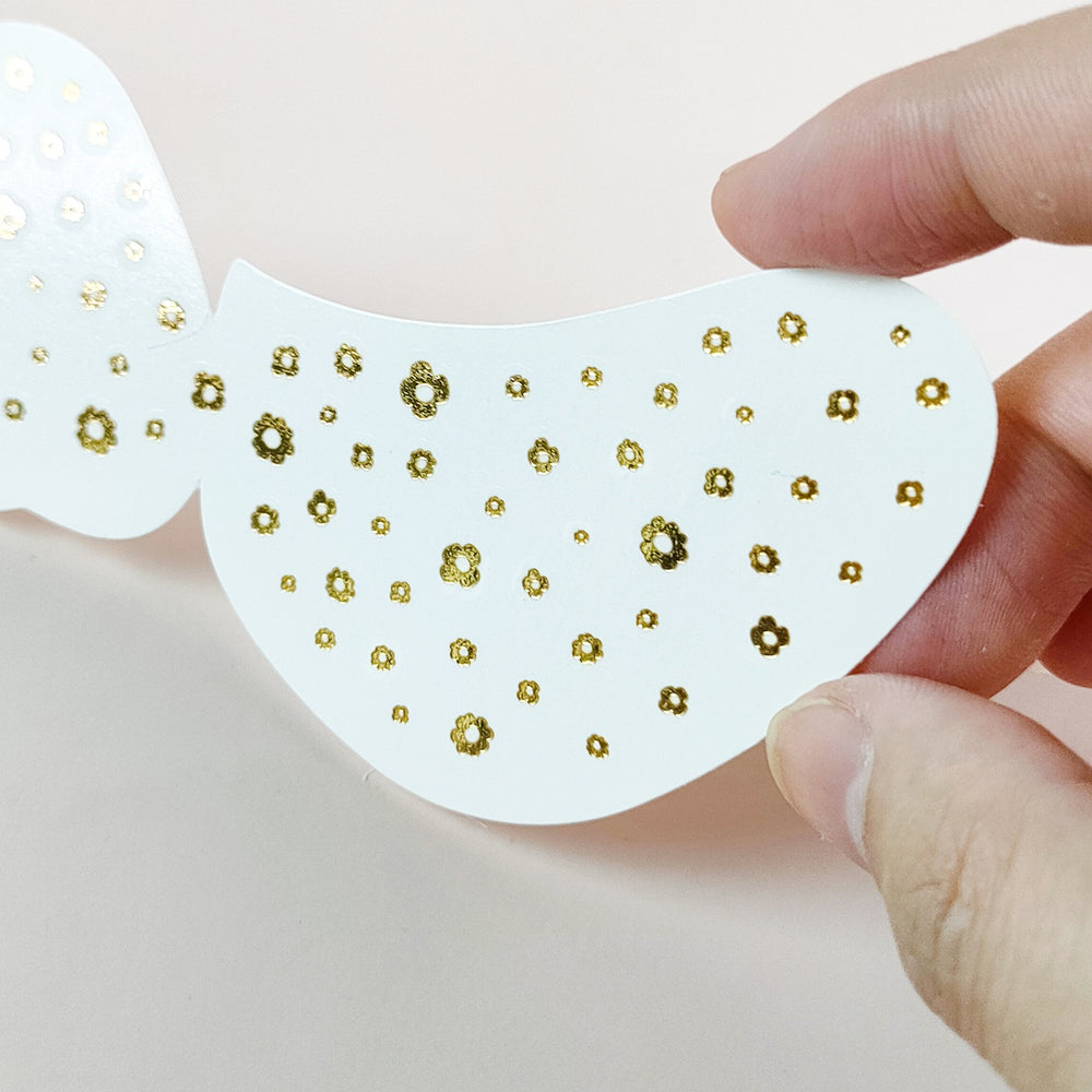 Hand holding a white patch with gold floral patterns on a light background