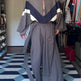 Person wearing a long, gray outfit with geometric patterns in a room with a checkered floor. 2
