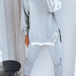 Person wearing a gray tracksuit with white accents in a minimalistic room.