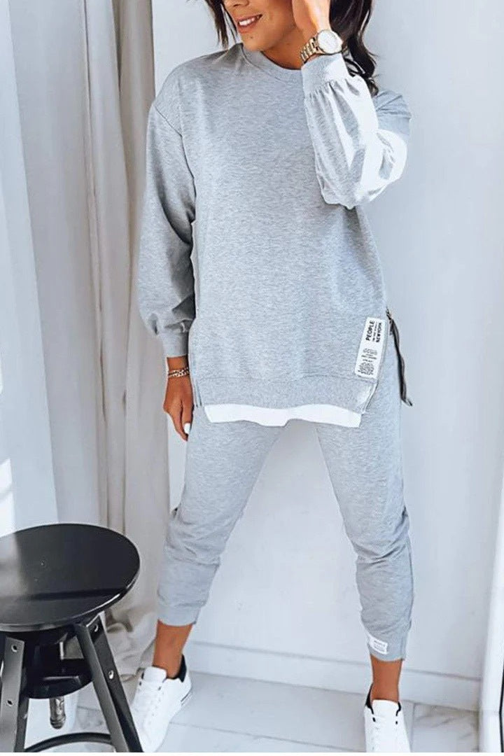 Person wearing a gray tracksuit with white accents in a minimalistic room.