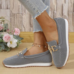 Gray patterned loafers worn with light blue jeans on a wooden floor.