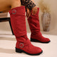 Red knee-high boots with metal buckles worn by a person, with a neutral background.