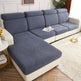 A sectional sofa with a chaise lounge in a bright living room. The sofa features textured slate blue seat and back cushions with cream-colored sides and base. Polar Fleece Sofa Cover – All-Season Universal Couch Slipcover (6 Colours, S–2XL)