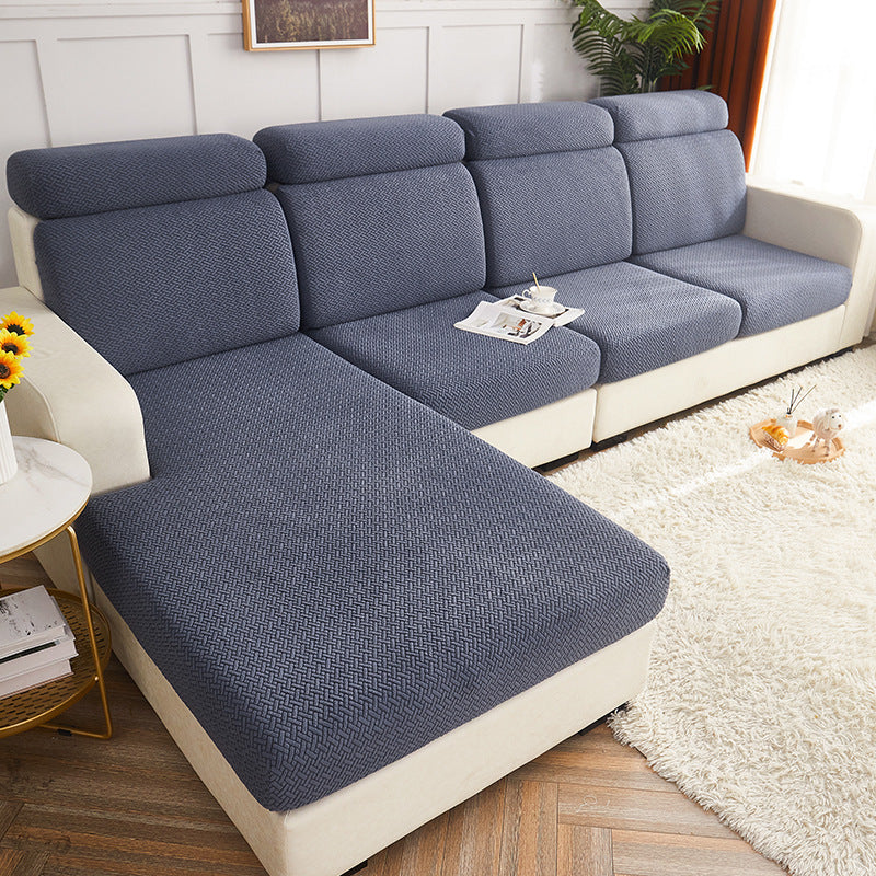A sectional sofa with a chaise lounge in a bright living room. The sofa features textured slate blue seat and back cushions with cream-colored sides and base. Polar Fleece Sofa Cover – All-Season Universal Couch Slipcover (6 Colours, S–2XL)