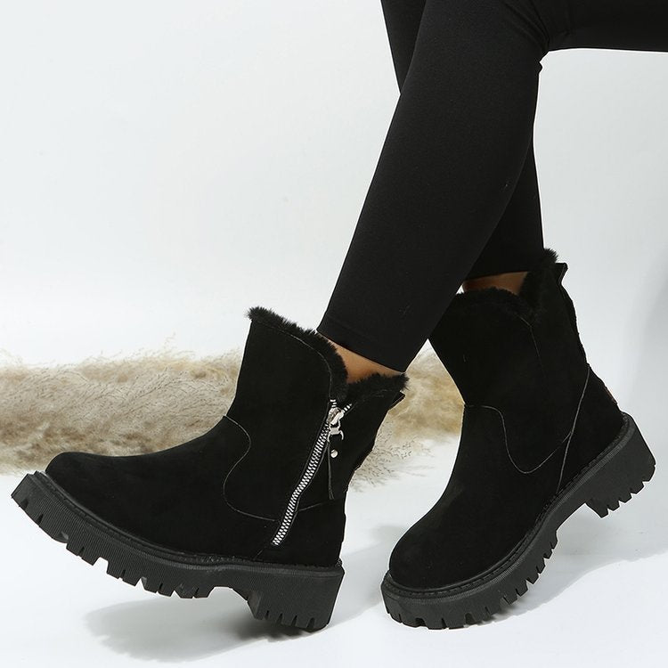 Black ankle boots with fur lining and zippers worn by a person on a light background