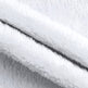 Close-up of a soft white plush or sherpa fabric with folded layers showing the fuzzy texture and a dark center seam.