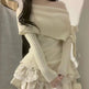 Woman wearing a beige off-shoulder knit cardigan over a dress with ruffled layers.