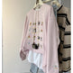 Pink sweatshirt with embroidered designs on a rack against a white wall
