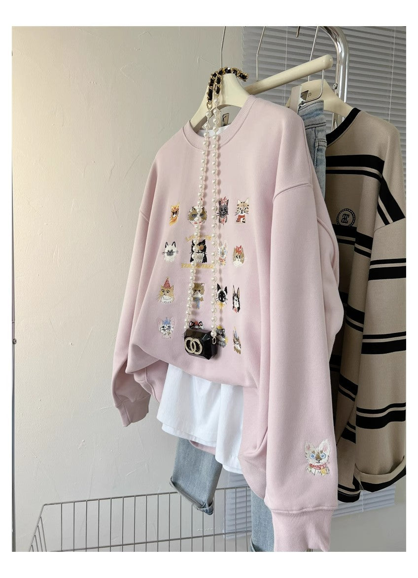 Pink sweatshirt with embroidered designs on a rack against a white wall